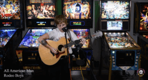 Tiff from Rodeo Boys playing live in front of pinball machines.